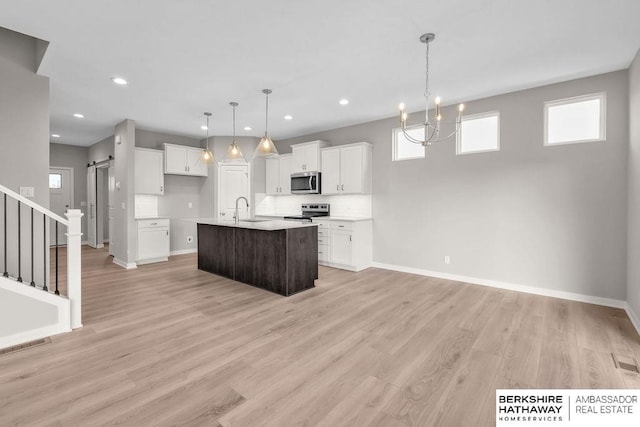 kitchen with a barn door, a center island with sink, stainless steel appliances, pendant lighting, and sink