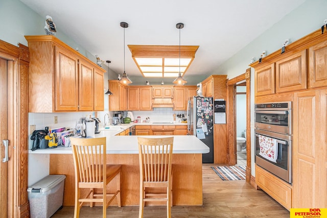 kitchen with light wood-type flooring, kitchen peninsula, a kitchen bar, appliances with stainless steel finishes, and decorative light fixtures