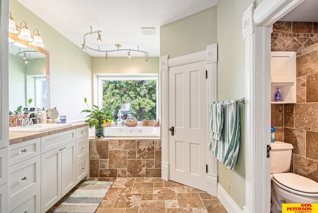 bathroom with tiled tub, vanity, toilet, and a textured ceiling