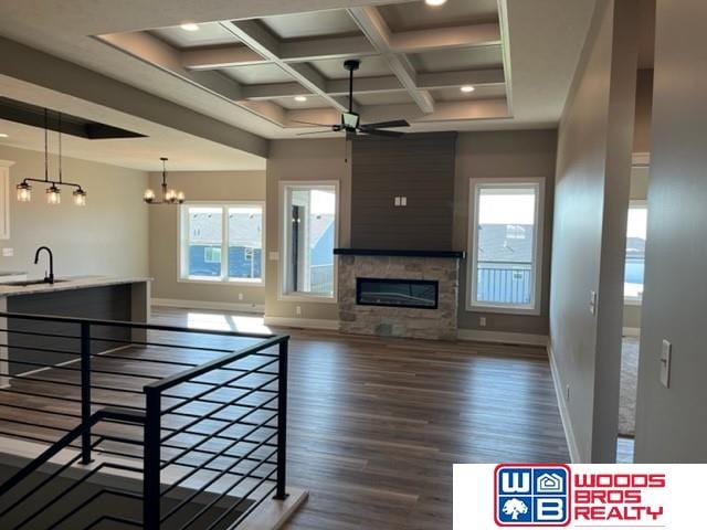 living room featuring ceiling fan with notable chandelier, a stone fireplace, dark hardwood / wood-style flooring, and plenty of natural light