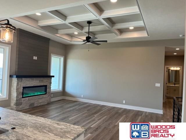 unfurnished living room featuring coffered ceiling, a stone fireplace, dark hardwood / wood-style flooring, beam ceiling, and ceiling fan