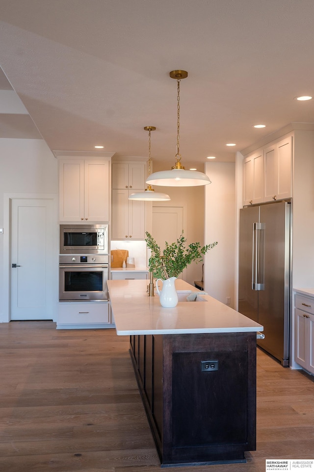 kitchen with white cabinets, appliances with stainless steel finishes, hanging light fixtures, and hardwood / wood-style floors