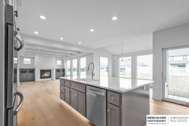 kitchen featuring stainless steel dishwasher, sink, a center island with sink, a notable chandelier, and fridge