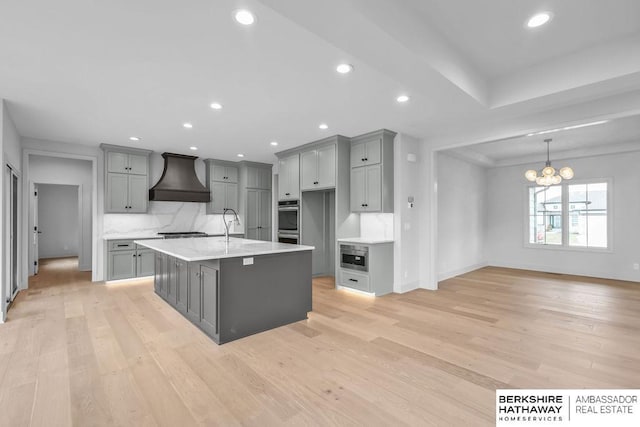 kitchen with custom range hood, light wood-type flooring, gray cabinets, and a notable chandelier