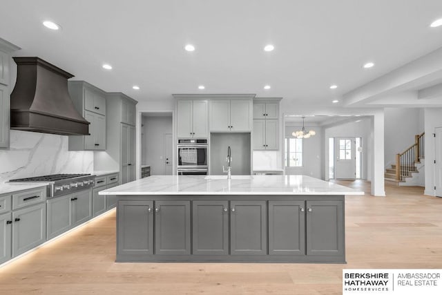 kitchen with gray cabinetry, a large island, appliances with stainless steel finishes, and custom exhaust hood