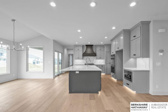 kitchen featuring backsplash, a center island with sink, hanging light fixtures, and wall chimney exhaust hood