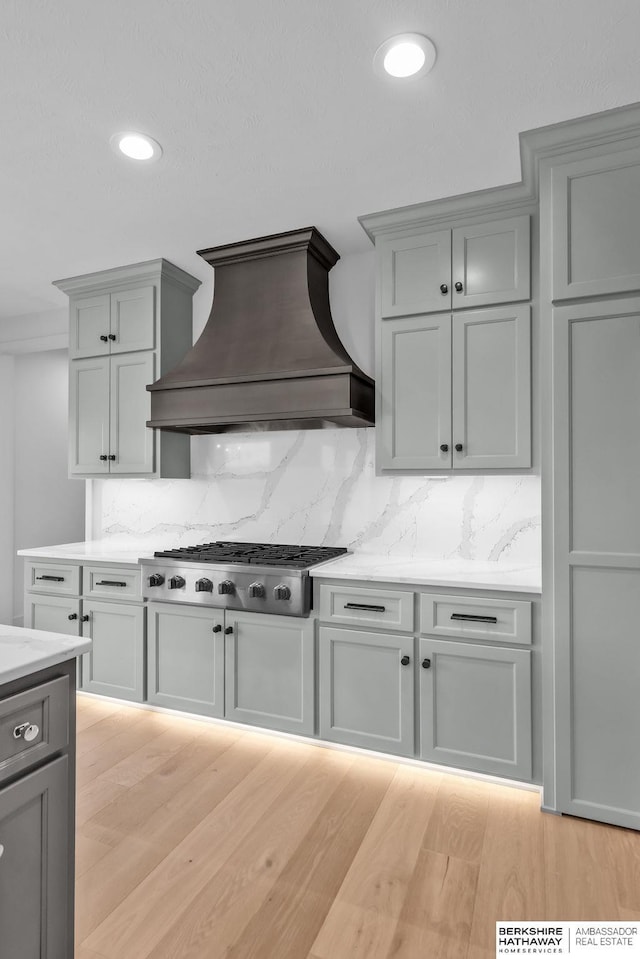 kitchen featuring decorative backsplash, gray cabinetry, custom exhaust hood, light hardwood / wood-style flooring, and stainless steel gas stovetop