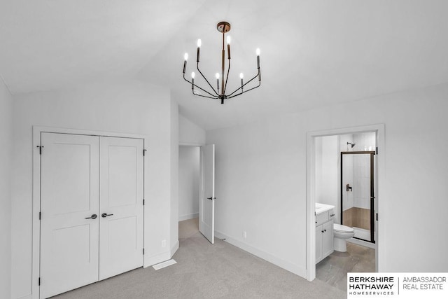 unfurnished bedroom featuring ensuite bathroom, a closet, light carpet, and vaulted ceiling