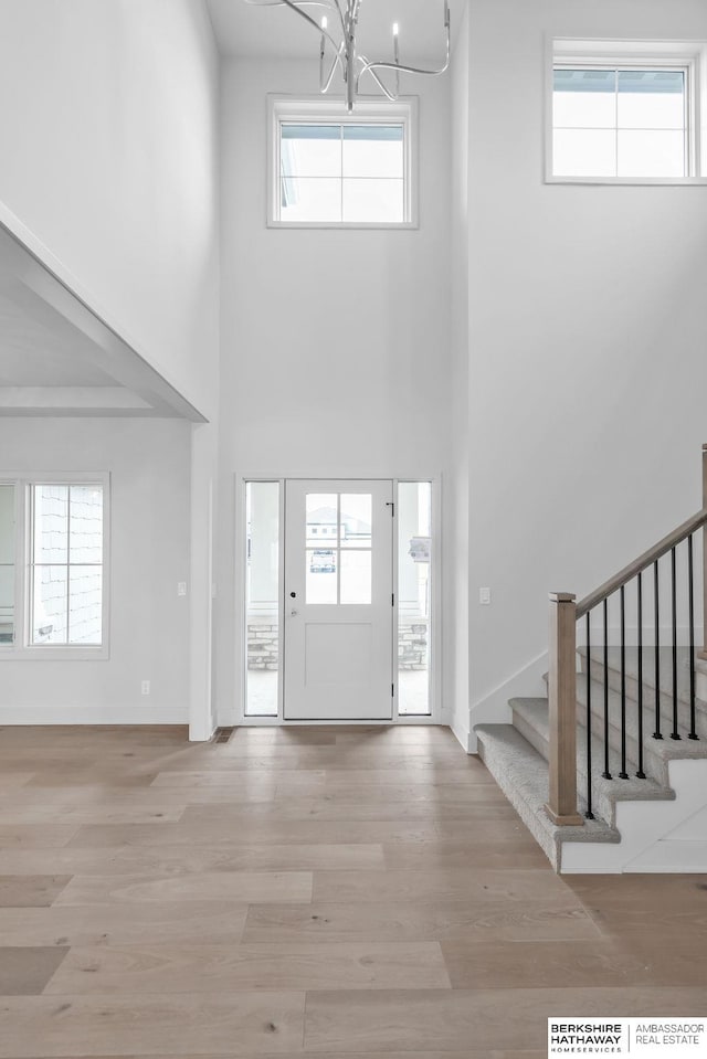 foyer entrance featuring light hardwood / wood-style flooring, a towering ceiling, and a notable chandelier