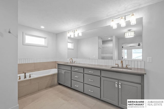 bathroom with tile patterned floors, tiled bath, ceiling fan, and vanity