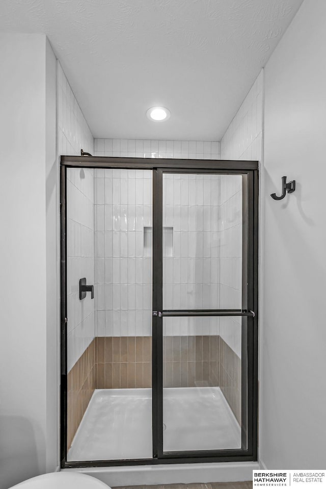 bathroom with a textured ceiling, toilet, and a shower with door