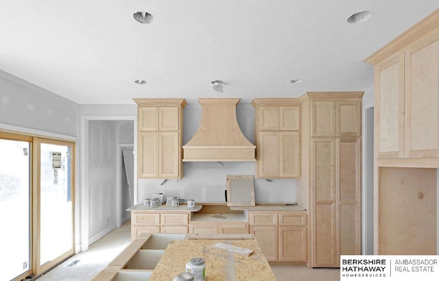 kitchen with light stone countertops, premium range hood, and light brown cabinetry