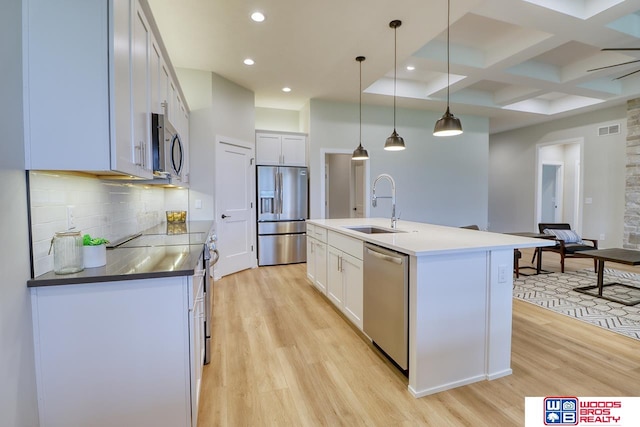 kitchen with appliances with stainless steel finishes, an island with sink, white cabinets, pendant lighting, and sink