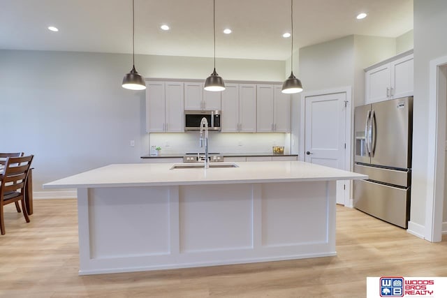 kitchen with decorative light fixtures, a kitchen island with sink, appliances with stainless steel finishes, and light hardwood / wood-style floors