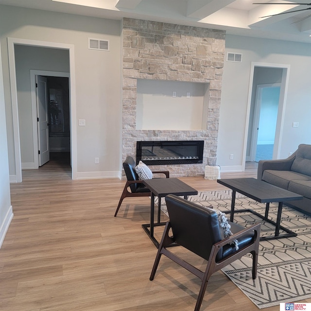 living room with light hardwood / wood-style floors, a stone fireplace, and ceiling fan