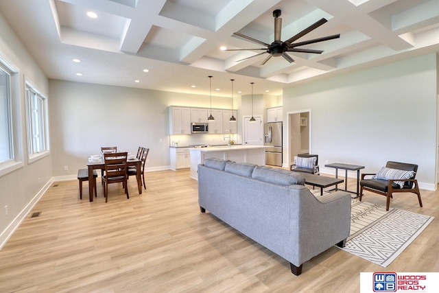 living room with light wood-type flooring, beamed ceiling, sink, coffered ceiling, and ceiling fan