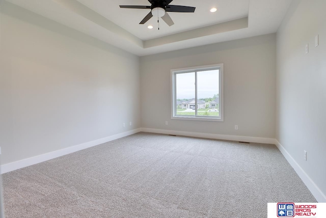 carpeted spare room featuring ceiling fan and a raised ceiling