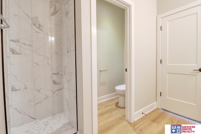 bathroom featuring a tile shower, wood-type flooring, and toilet