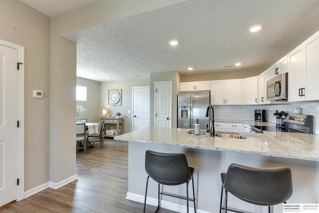 kitchen featuring kitchen peninsula, wood-type flooring, white cabinetry, appliances with stainless steel finishes, and light stone countertops