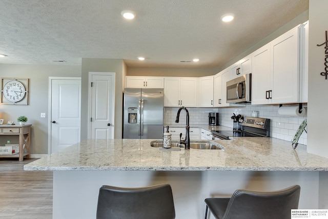 kitchen with kitchen peninsula, light hardwood / wood-style flooring, white cabinetry, appliances with stainless steel finishes, and a breakfast bar area