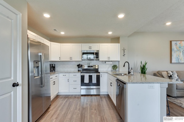 kitchen featuring sink, stainless steel appliances, kitchen peninsula, and white cabinetry