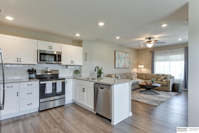 kitchen with appliances with stainless steel finishes, kitchen peninsula, light hardwood / wood-style floors, and white cabinets