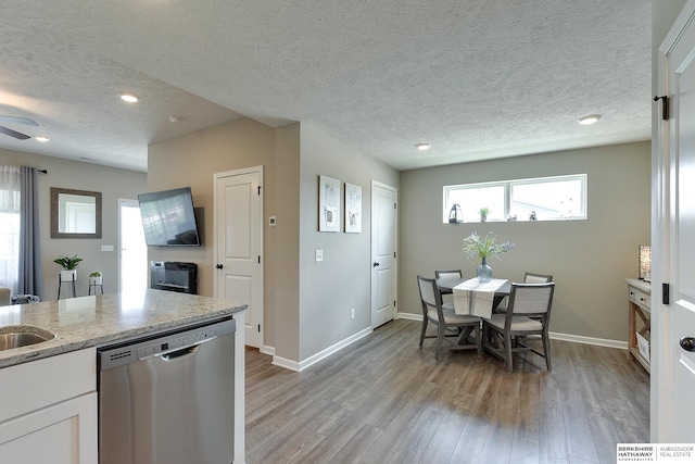 kitchen with light hardwood / wood-style floors, white cabinetry, light stone countertops, a textured ceiling, and stainless steel dishwasher