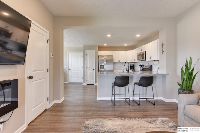 kitchen with appliances with stainless steel finishes, hardwood / wood-style floors, kitchen peninsula, and white cabinetry