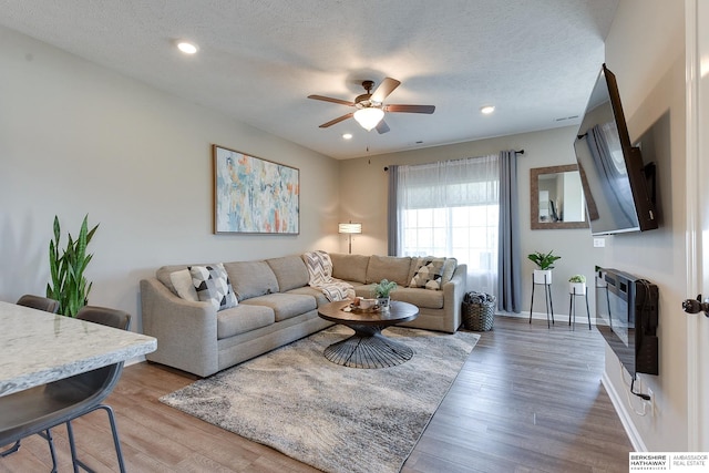 living room with heating unit, ceiling fan, hardwood / wood-style flooring, and a textured ceiling