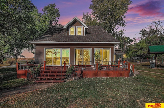 back house at dusk featuring a wooden deck and a yard