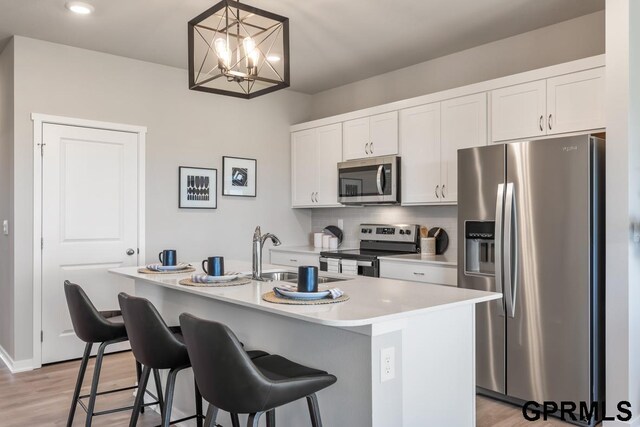 kitchen featuring decorative light fixtures, a center island with sink, appliances with stainless steel finishes, and white cabinetry