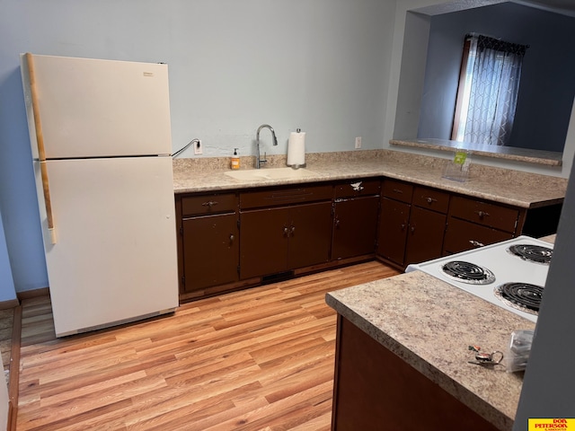 kitchen with white appliances, kitchen peninsula, light wood-type flooring, dark brown cabinetry, and sink