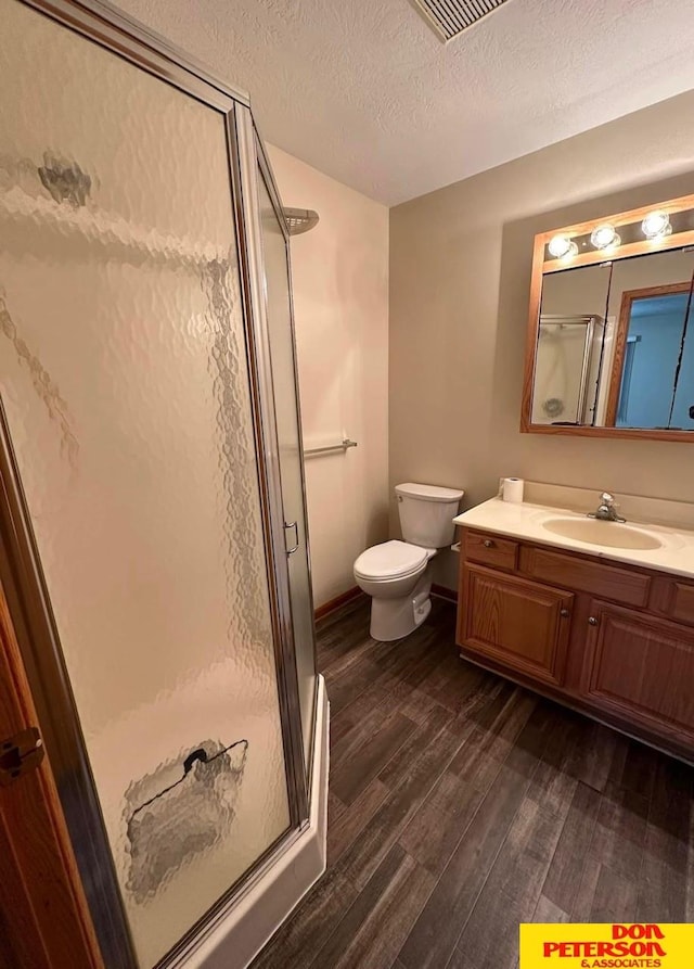 bathroom with walk in shower, a textured ceiling, wood-type flooring, vanity, and toilet