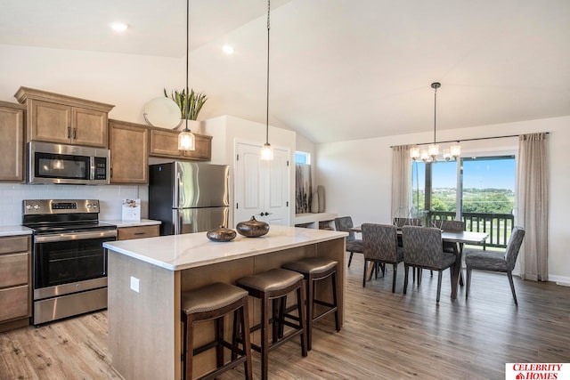 kitchen with appliances with stainless steel finishes, hanging light fixtures, light hardwood / wood-style floors, a kitchen island, and an inviting chandelier