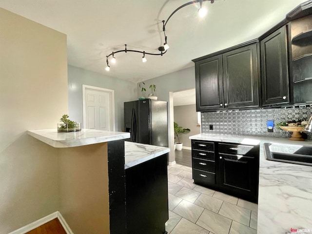 kitchen featuring sink, tasteful backsplash, track lighting, black refrigerator with ice dispenser, and light stone countertops