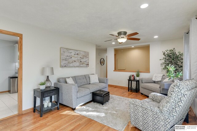 living room with light hardwood / wood-style floors, ceiling fan, and a textured ceiling