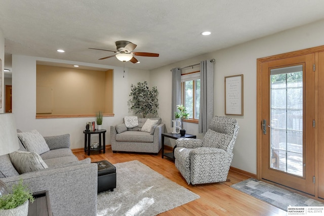 living room with light wood-type flooring, ceiling fan, and a textured ceiling