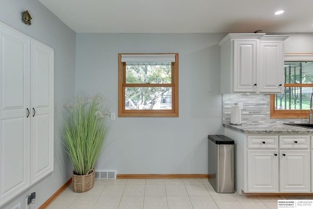 kitchen with light tile patterned flooring, light stone counters, white cabinets, backsplash, and sink