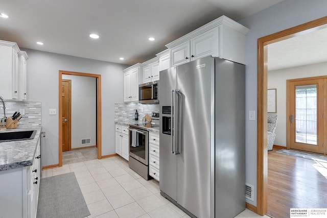 kitchen with light hardwood / wood-style floors, tasteful backsplash, white cabinets, light stone countertops, and stainless steel appliances