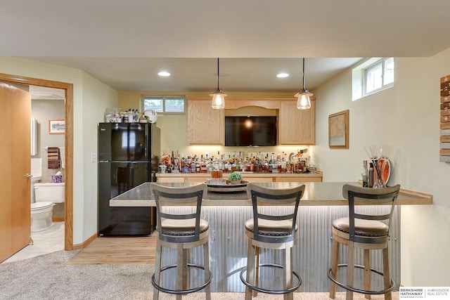 kitchen with a breakfast bar area, light tile patterned floors, decorative light fixtures, black refrigerator, and light brown cabinetry