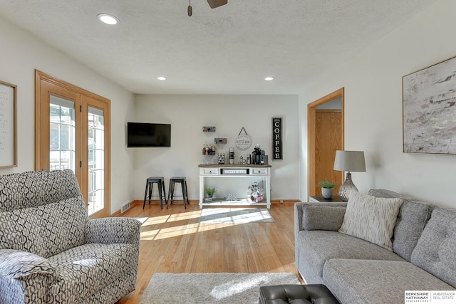 living room featuring a textured ceiling, light hardwood / wood-style floors, and ceiling fan