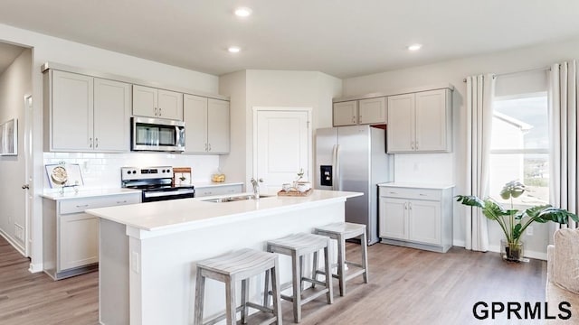 kitchen with appliances with stainless steel finishes, light wood-type flooring, a kitchen bar, a center island with sink, and sink