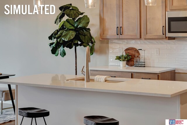 kitchen featuring sink, light brown cabinets, a kitchen breakfast bar, backsplash, and decorative light fixtures