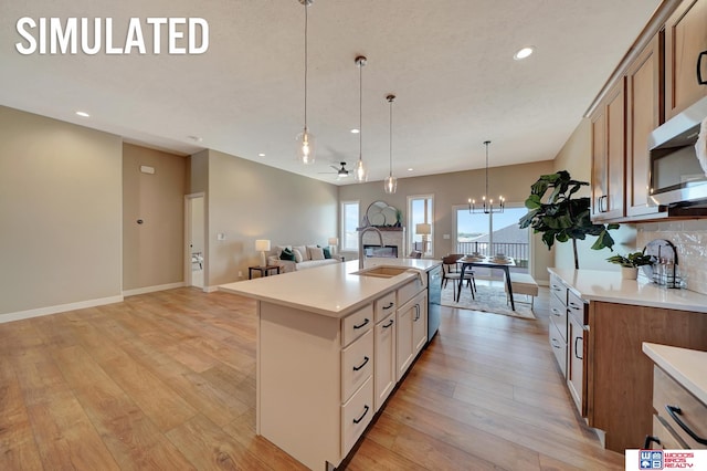 kitchen featuring ceiling fan with notable chandelier, sink, decorative light fixtures, a center island with sink, and light hardwood / wood-style floors