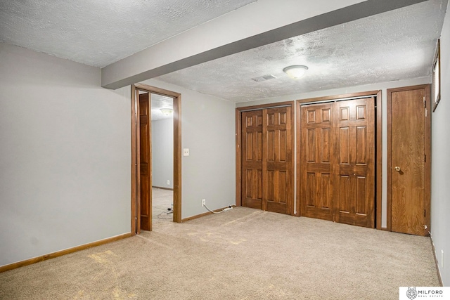 unfurnished bedroom featuring a textured ceiling, two closets, and light colored carpet