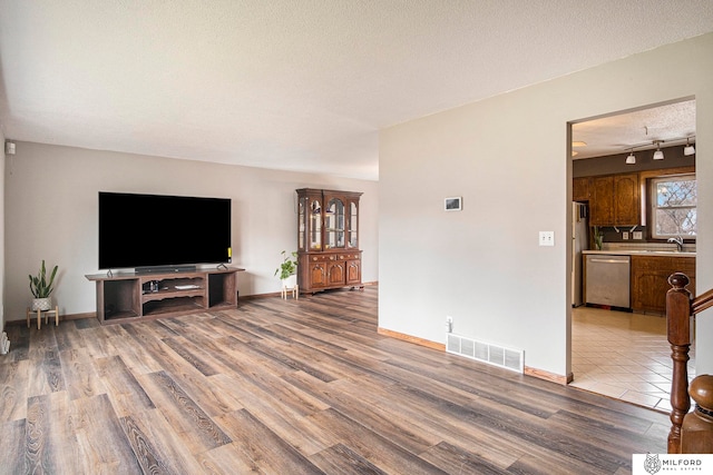 living room featuring rail lighting, a textured ceiling, hardwood / wood-style floors, and sink