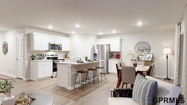 kitchen with a kitchen breakfast bar, light hardwood / wood-style floors, white cabinets, stainless steel appliances, and a center island with sink