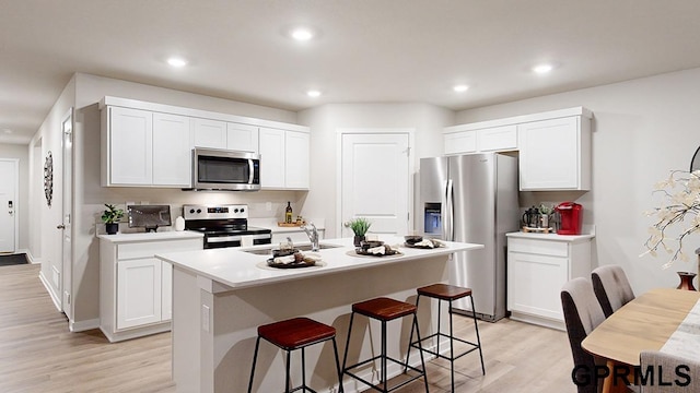 kitchen featuring light hardwood / wood-style flooring, stainless steel appliances, white cabinets, and a center island with sink