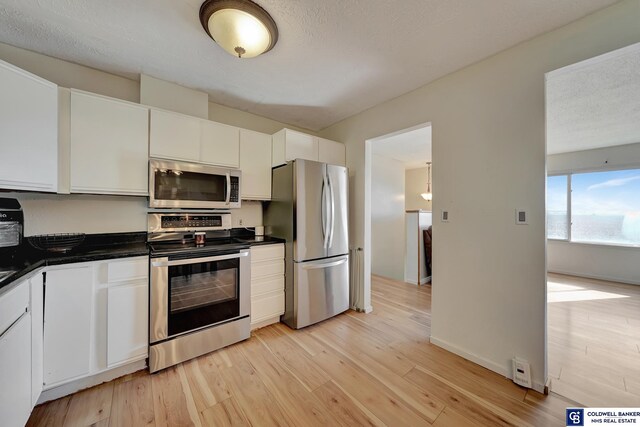 kitchen featuring white cabinets, a textured ceiling, stainless steel appliances, and light hardwood / wood-style floors