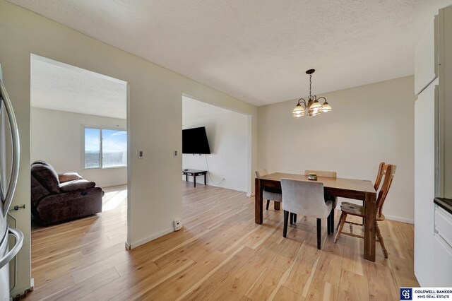 dining area with a textured ceiling, a chandelier, and light hardwood / wood-style floors